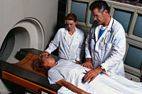 Picture of a patient in a CT scanner, with a physician and a technologist present